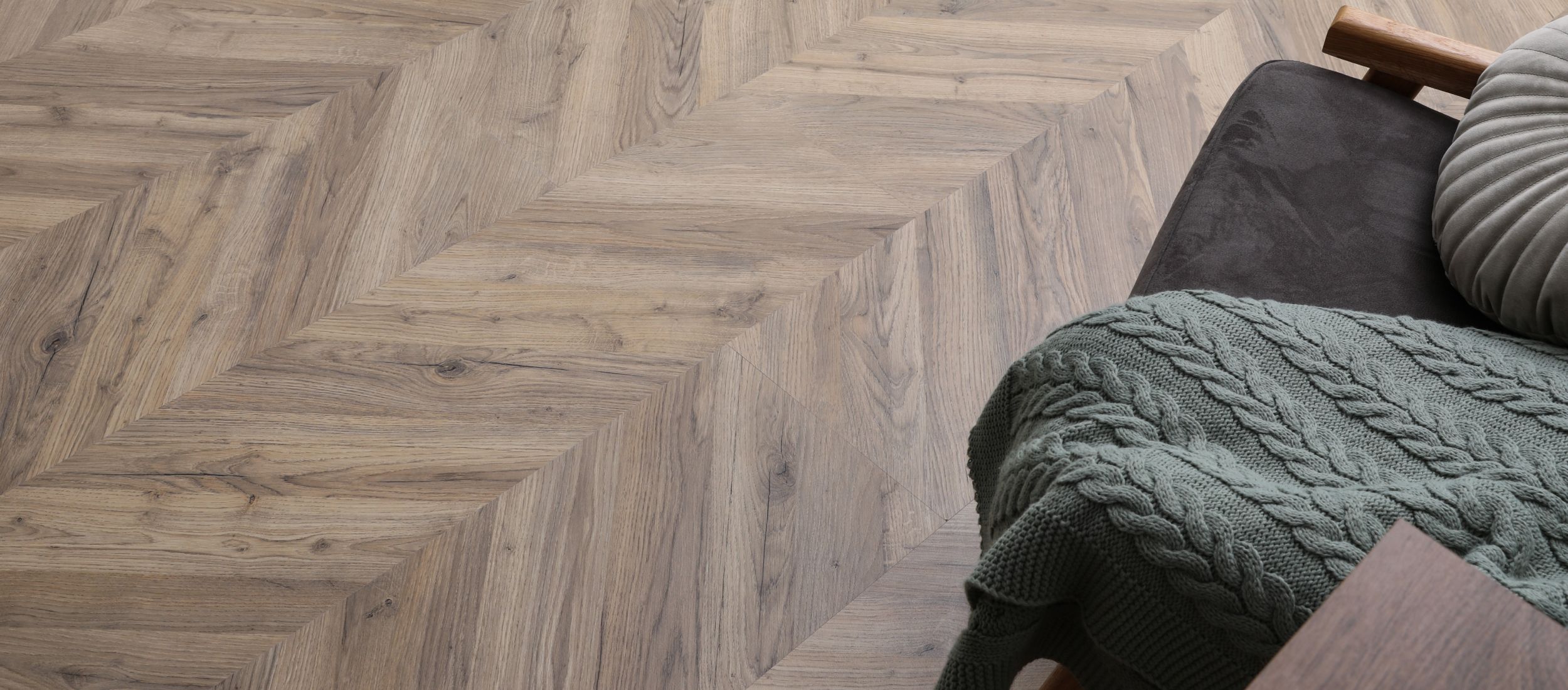 Heller Parkettboden in Fischgrätmuster mit Couch und Decke im Wohnzimmer.